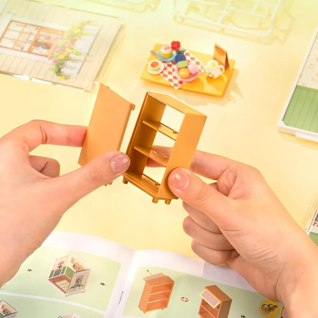 Miniature wooden furniture set with hands opening a box on a yellow background