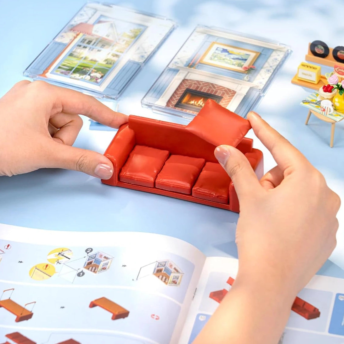 Red toy sofa being assembled on a blue surface with a book of illustrations.