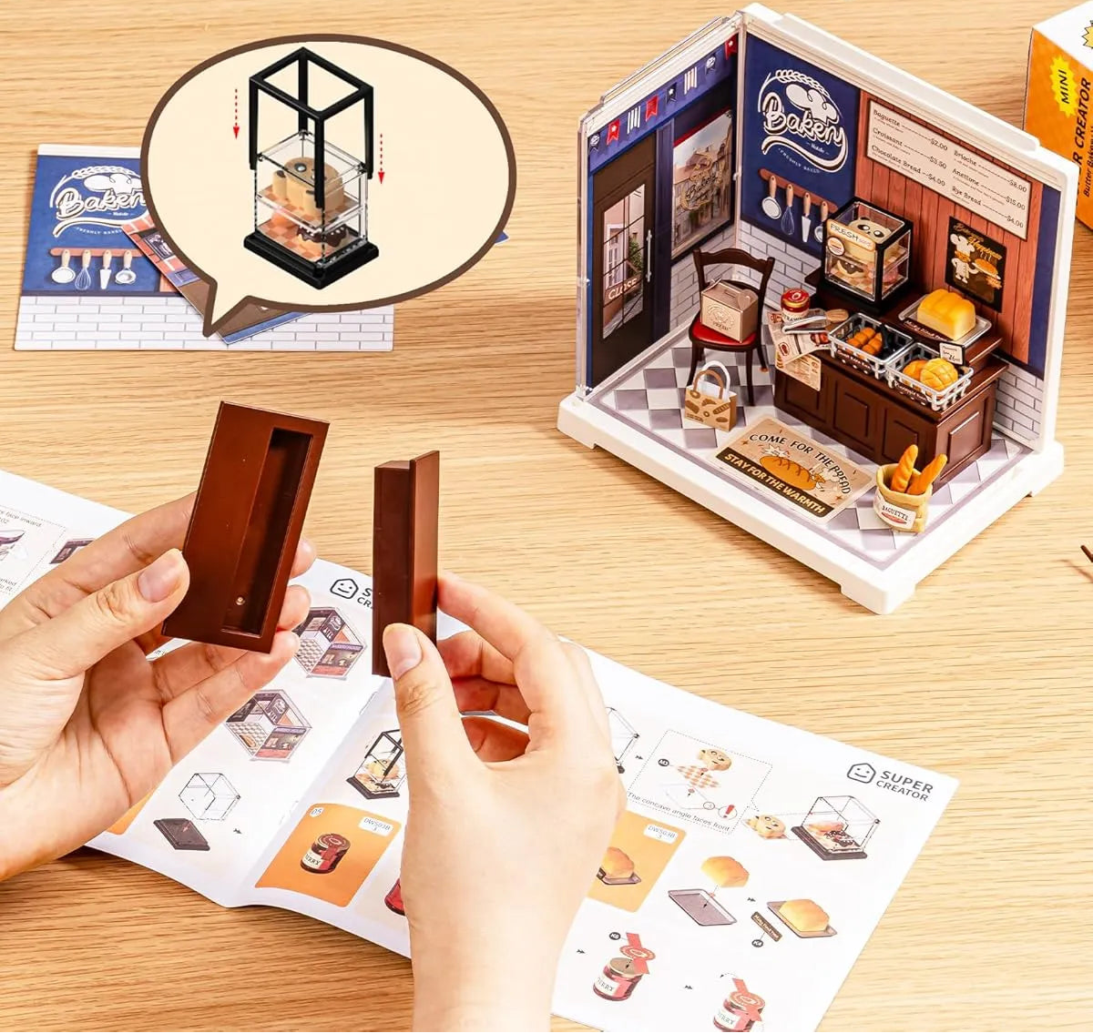 Unboxing a miniature model of a bakery with packaging and instructions on a wooden surface.